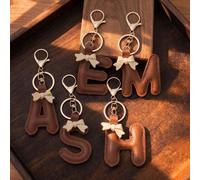 1 pièce Porte-clés à la mode en PU avec lettre, comprenant un mousqueton, un nœud papillon et un pendentif. Convient pour la décoration de sacs et l'accrocher à un sac à dos. Adapté pour un usage quot