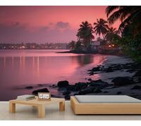 Fresque murale représentant un coucher de soleil tropical rose sur une plage, avec palmiers et village côtier, idéale pour une ambiance de chambre ou de salon. 150x105cm (Non autocollant)