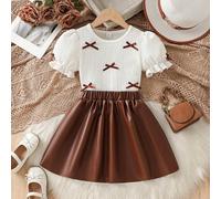 Nouvel arrivage d'été, ensemble élégant de mode européenne et américaine pour jeunes filles. T-shirt à col rond, manches bouffantes avec décoration de nœud + jupe en PU. Convient pour le quotidien, le