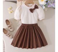 Nouvel ensemble d'été mode européenne et américaine élégant pour filles et tout-petits, top T-shirt à manches courtes bouffantes avec col rond et décoration nœud + jupe, style quotidien, trajet, école