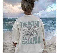 T-shirt court en coton blanc, version classique ample, avec le texte "L'OCÉAN M'APPELLE" imprimé à l'arrière avec l'image d'une tortue de mer, faisant écho au thème de l'océan pour transmettre le dési